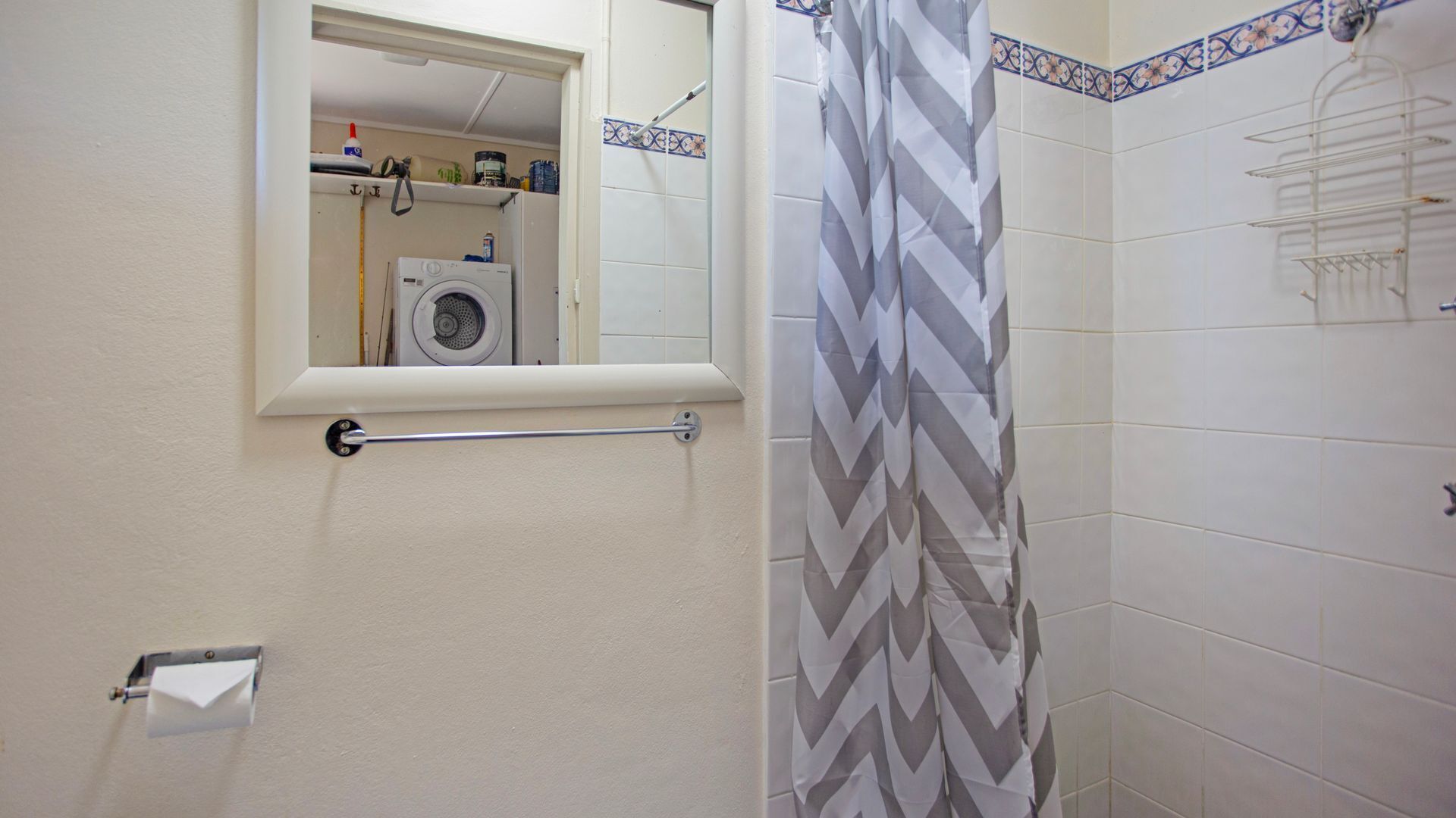 A bathroom with a shower, a hanging towel rack, a small window, and a mirror.