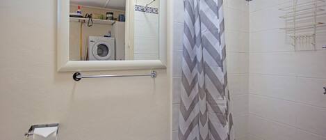 A bathroom with a shower, a hanging towel rack, a small window, and a mirror.