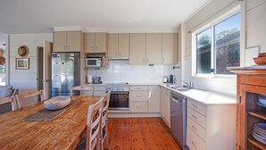 A kitchen with wooden flooring, white cabinets, a microwave, a stove, a sink, and a window.