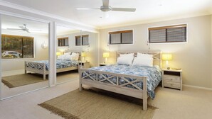 Un dormitorio con cama, dos mesitas de noche, un espejo y un ventilador de techo.