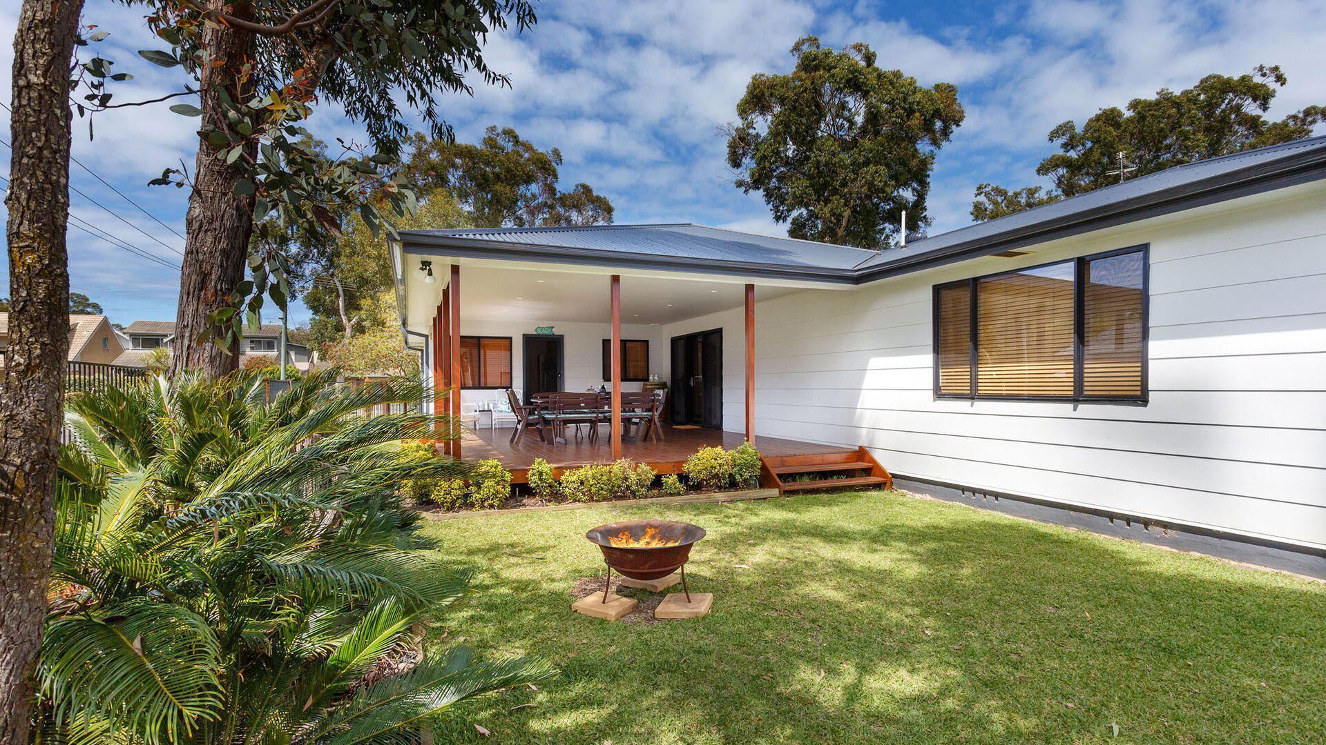 Une maison moderne dotée d’un patio couvert, d’un foyer extérieur et d’une pelouse bien entretenue.