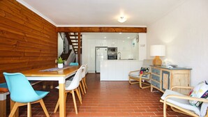 Cuina compacta amb armaris blancs, una illa central i zona menjador amb taula de fusta i cadires blaves.