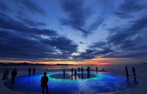 A circular illuminated platform with people standing around it, set against a sunset sky. - House with outdoor pool - Perfect for families! (Murvica)