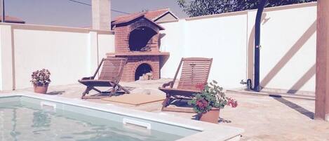 A pool area with lounge chairs and a brick oven.