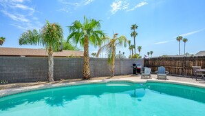 A swimming pool with a wooden fence, palm trees, and outdoor furniture. - Cozy, private getaway with pool (Mesa)