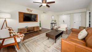 A living room with a flat-screen TV, wooden entertainment unit, leather sofa, and a ceiling fan. - Cozy, private getaway with pool (Mesa)