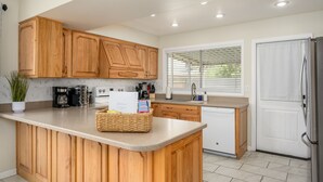 A kitchen with wooden cabinets, a central island, a refrigerator, and a window with blinds. - Cozy, private getaway with pool (Mesa)