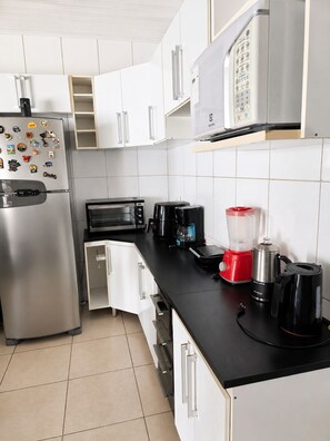 Moderni keittiö, jossa on valkoiset kaapit, ruostumattomasta teräksestä valmistettu jääkaappi, mikroaaltouuni, kahvinkeitin, tehosekoitin ja leivänpaahdin.