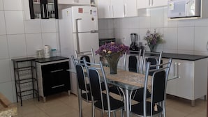 Une cuisine moderne avec des meubles blancs, une table à manger avec des chaises, un réfrigérateur, un four à micro-ondes et un petit plan de travail noir avec un évier.