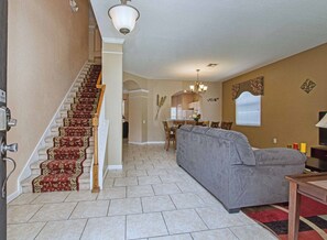 A spacious living area with a staircase, a grey sofa, and a dining area in the background.