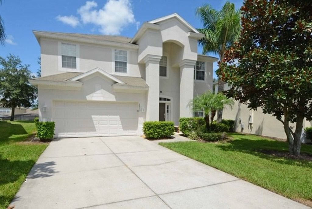 A two-story house with a central garage, surrounded by well-maintained lawns and a few trees.
