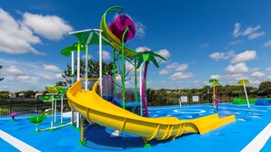 Ein Wasserpark mit einer gelben Rutsche, verschiedenen Wasserspielen und einem blau gestalteten Poolbereich.