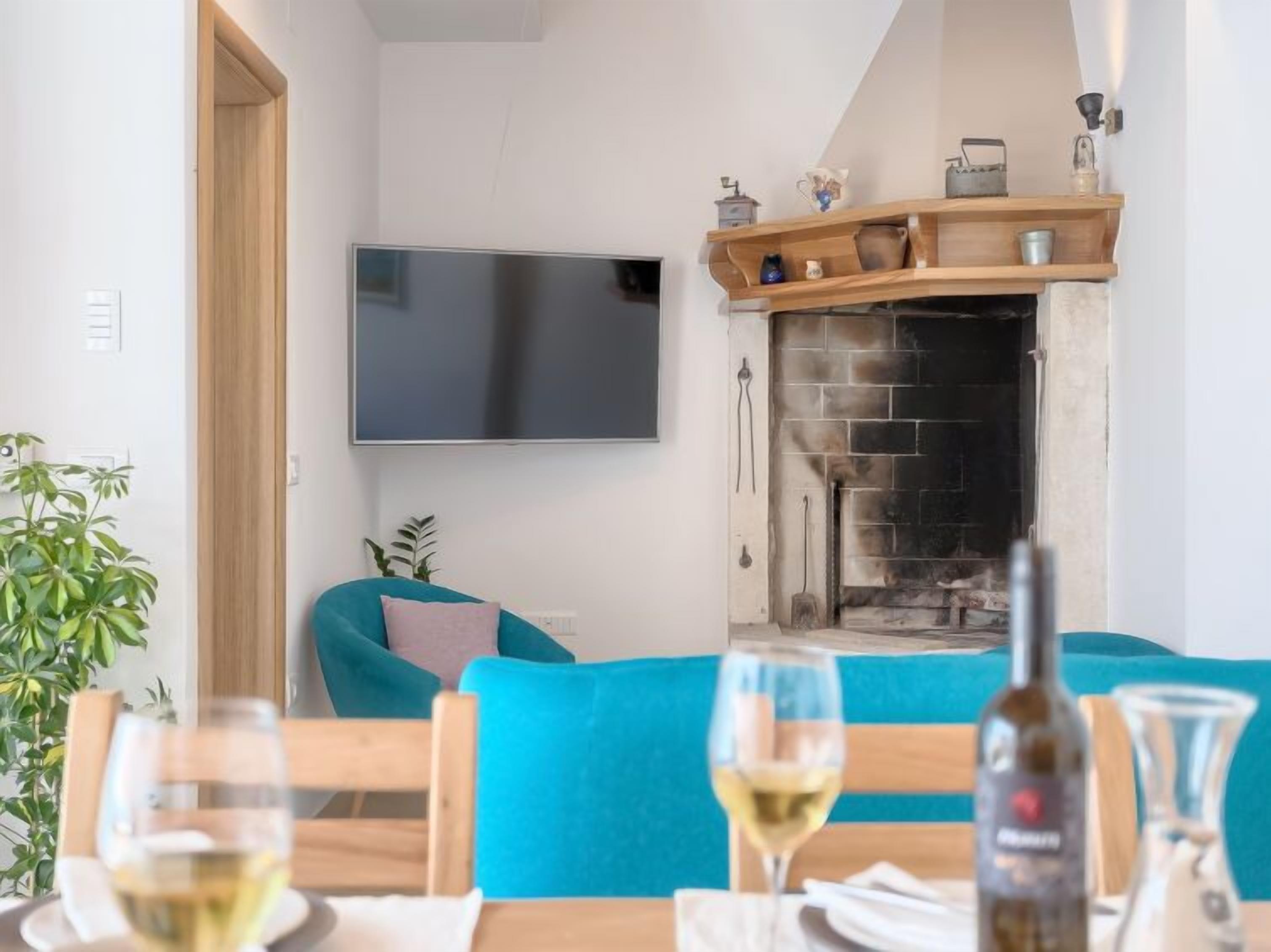 Een gezellige woonkamer met een open haard, een flatscreen-televisie aan de muur en een eethoek met een tafel gedekt voor twee personen.