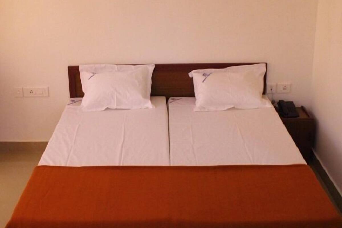 A double bed with white linens and two pillows, a wooden headboard, and a nightstand with a phone.