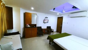 Habitación de hotel con cama, sofá, escritorio con silla, armario, ventilador de techo y aire acondicionado.