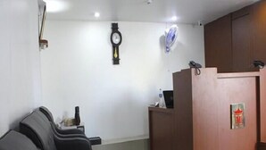 Una zona de recepción con un escritorio de madera, un reloj y una fila de sillas negras.