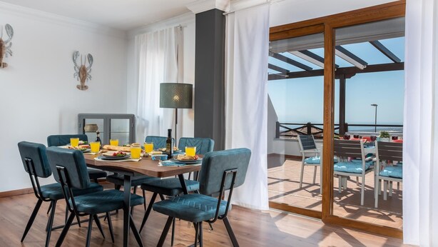 A dining area with a table set for four, a large window with curtains, and a view of the sea. - 1. Villa Conde prívate pool,sea view & barbacue (Adeje)