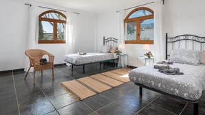 A hotel room with two beds, a wicker chair, a small table with lamps, and a view of the outdoors through large windows. - 1. Villa Conde prívate pool,sea view & barbacue (Adeje)