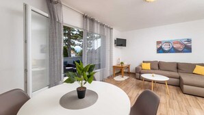 A modern living room with a sofa, a coffee table, a TV mounted on the wall, and a large window with curtains. - Apartment LaPePa (Silo - island Krk)