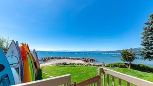 A view of a beach with surfboards lined up on the left, a grassy area in the middle, and a wooden staircase leading down to the beach. - Ideal Couple, Small Family Getaway, Lakefront Complex w/ Private Beach/Pool by Tahoe Time VR (Tahoe Vista)
