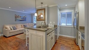 A modern kitchen with a central island, white cabinetry, and a dining area with a sofa. - Ideal Couple, Small Family Getaway, Lakefront Complex w/ Private Beach/Pool by Tahoe Time VR (Tahoe Vista)