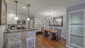 A kitchen with white cabinets, a wooden dining table, and pendant lights. - Ideal Couple, Small Family Getaway, Lakefront Complex w/ Private Beach/Pool by Tahoe Time VR (Tahoe Vista)