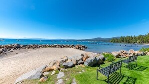 A beach with a rocky shoreline, a clear blue sky, and a view of the sea with boats. - Ideal Couple, Small Family Getaway, Lakefront Complex w/ Private Beach/Pool by Tahoe Time VR (Tahoe Vista)