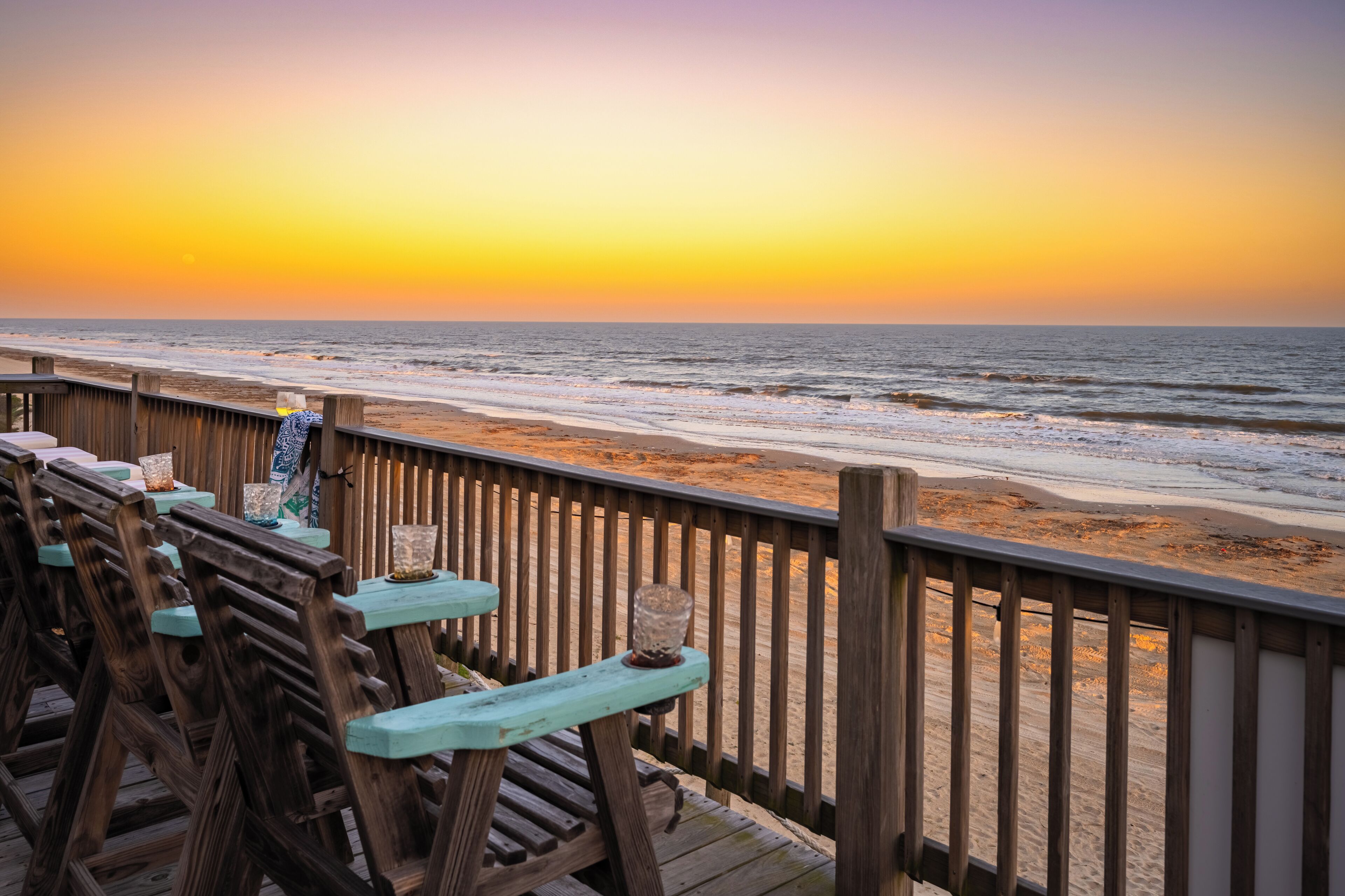 A wooden deck with benches overlooking a beach at sunset.