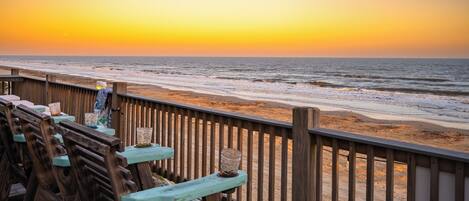 A wooden deck with benches overlooking a beach at sunset.