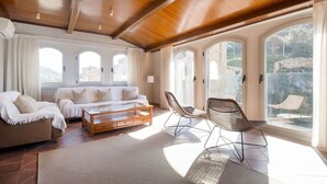 A spacious living area with a wooden ceiling, a sofa, two chairs, a coffee table, and large windows offering a view of the outdoors. - Luxury Rocamar – Beachfront & Terrace (Tossa De Mar)