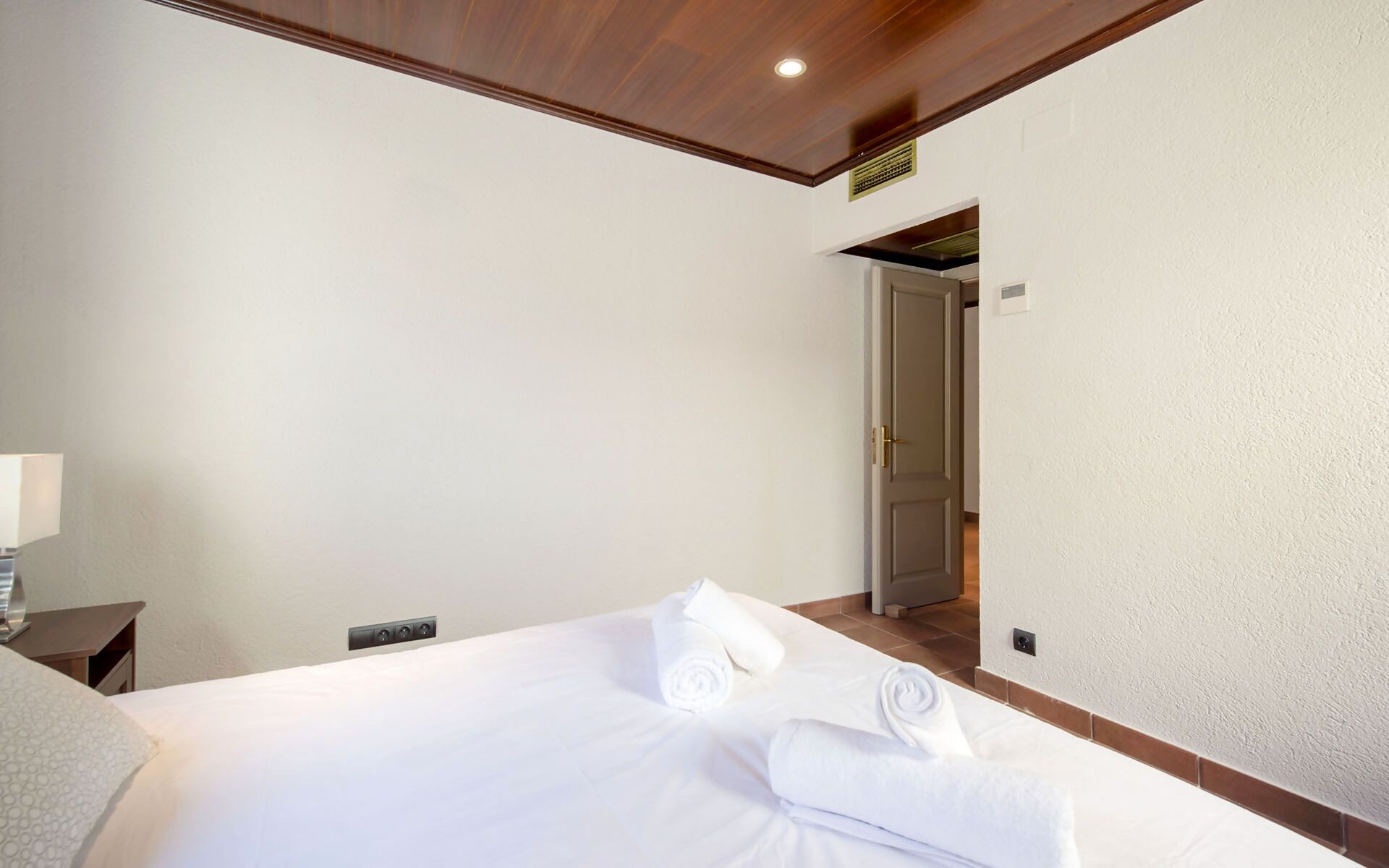 Une chambre d’hôtel avec un lit, une table de chevet, une lampe et une porte donnant sur une autre pièce.