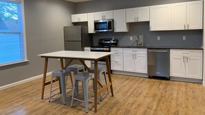 A modern kitchen with white cabinets, stainless steel appliances, and a wooden table with stools. - New 2 Bed 2Bath Spacious Apartment w/Deck & Parking (Pittsburgh)
