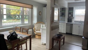Een moderne keuken met witte kasten, een eethoek met een houten tafel en stoelen, en uitzicht op groen.