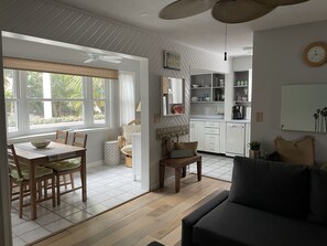 Relax in this open-plan living space with a dining area and kitchen, featuring a large window, ceiling fan, and comfortable seating options.
