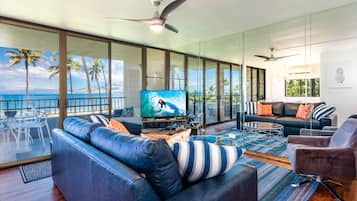 A modern living room with a large TV, leather sofas, and a view of the ocean.