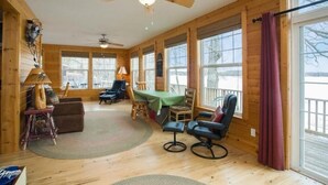 Un intérieur de chalet chaleureux avec des murs en bois, un ventilateur de plafond, une table à manger avec des chaises et de grandes fenêtres.
