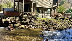 Eine zweistöckige Holzhütte mit Balkon, gelegen an einem Bach mit Steinen und Moos.