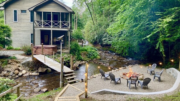 Eine rustikale Holzhütte mit einer Veranda, einem Feuerstellenbereich mit Sitzgelegenheiten und einem nahen Bach.