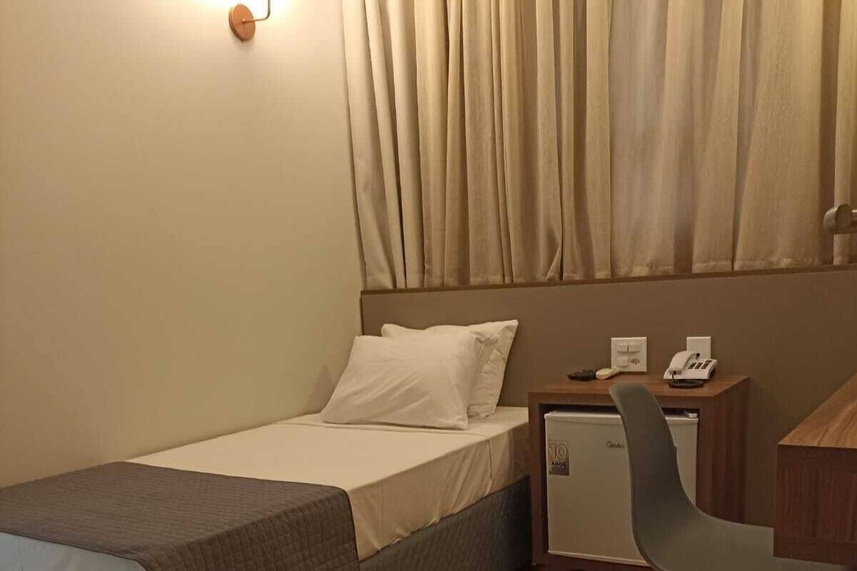 Ein Hotelzimmer mit Bett, Schreibtisch mit Stuhl, Nachttisch und Wandlampe.