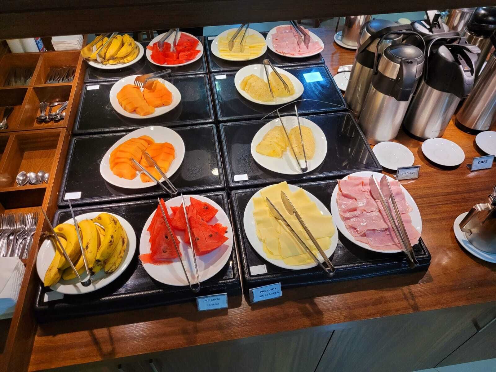 A buffet with various food items like bananas, watermelon, cheese, and ham.