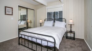 A bedroom with a metal bed frame, white bedding, two bedside lamps, a large mirror, and a framed quote on the wall. - Escape to Bearadise - Close to Slopes, Shuffleboard, Fireplace, BBQ (Big Bear Lake)