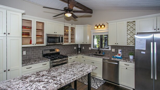 A modern kitchen with white cabinets, granite countertops, a stainless steel refrigerator, and a ceiling fan. - Escape to Bearadise - Close to Slopes, Shuffleboard, Fireplace, BBQ (Big Bear Lake)