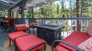 A covered outdoor seating area with red cushioned chairs and a fire feature. - Escape to Bearadise - Close to Slopes, Shuffleboard, Fireplace, BBQ (Big Bear Lake)