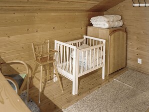 Una habitación de madera con una cuna, una silla de madera y un armario.