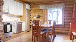 A log cabin interior with a kitchen, dining area, and a large window.