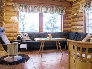 Un interior acogedor de cabaña de madera con un sofá, un sillón y una mesita con una vela.