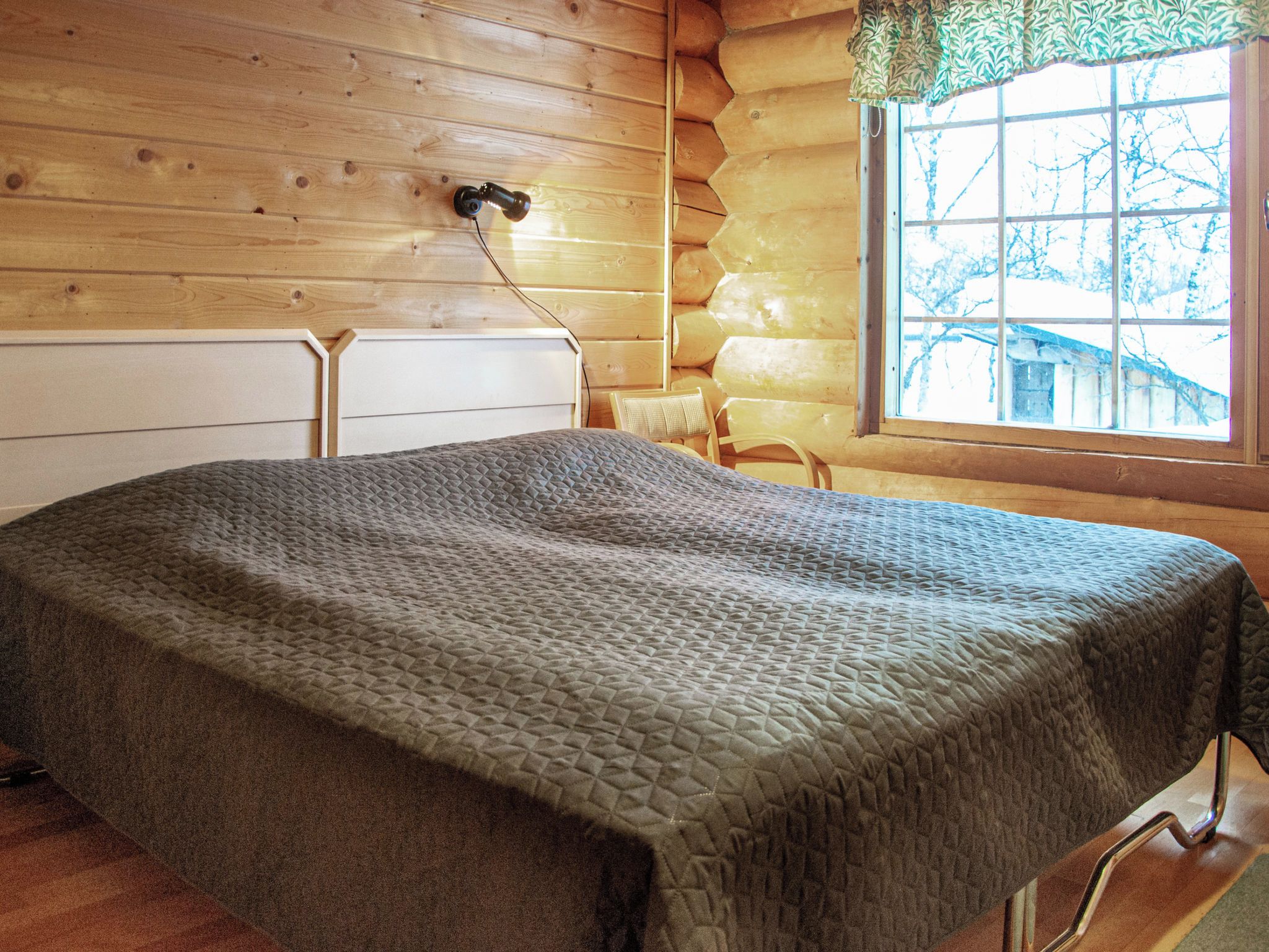 Una camera in legno con un letto, una finestra e una sedia.