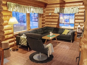 L’intérieur d’un chalet confortable, avec un canapé d’angle, une petite table et une lampe.