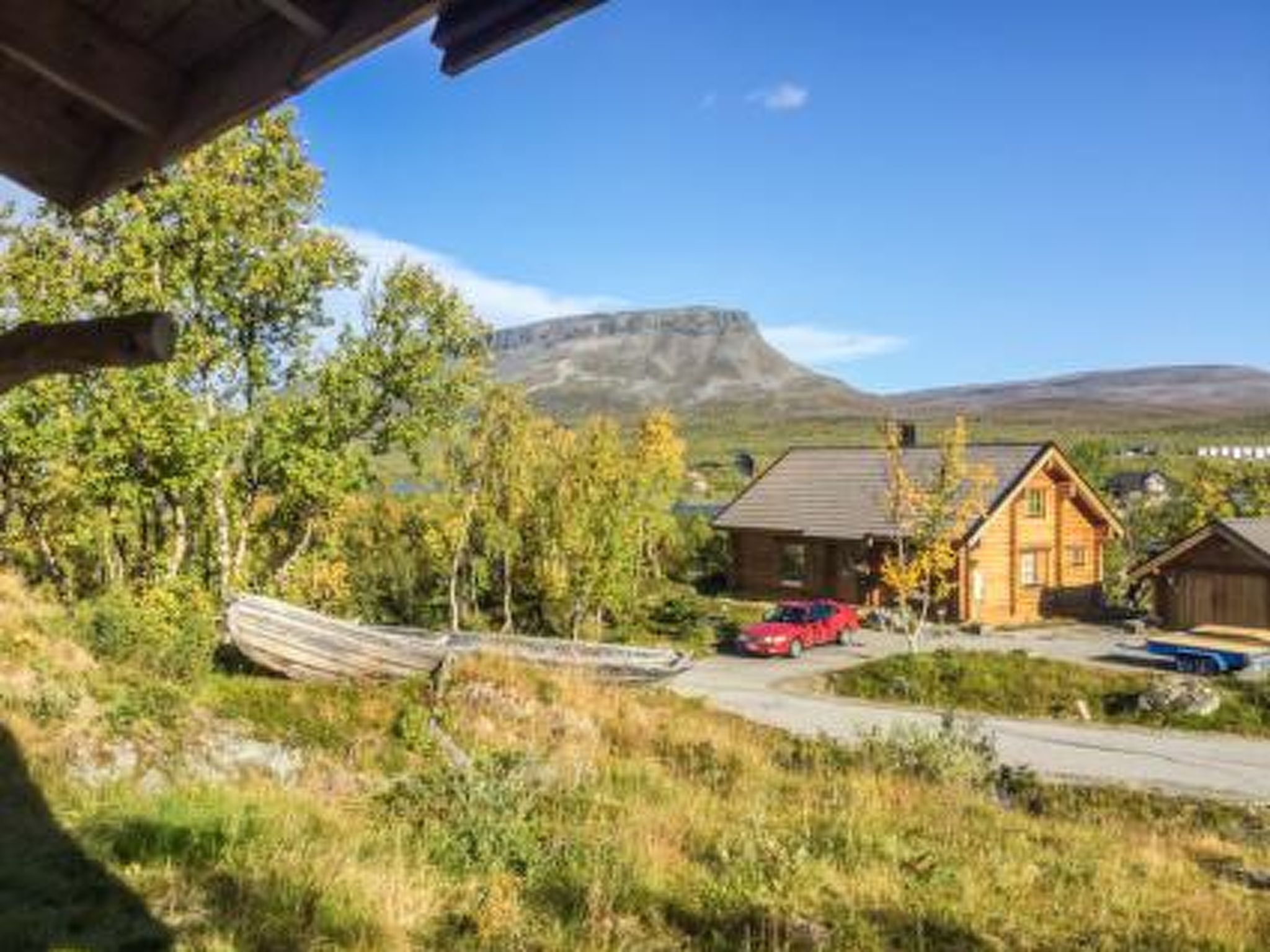 A cabin with a wooden exterior, a red car parked in front, and a mountainous backdrop.