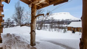 A wooden cabin with a snow-covered landscape and a mountain in the background.